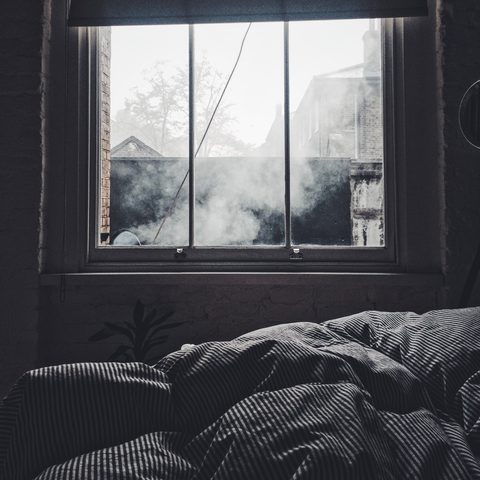 A rumpled bed under a window with soft morning light
