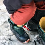 Green hiking boots being laced on snowy ground