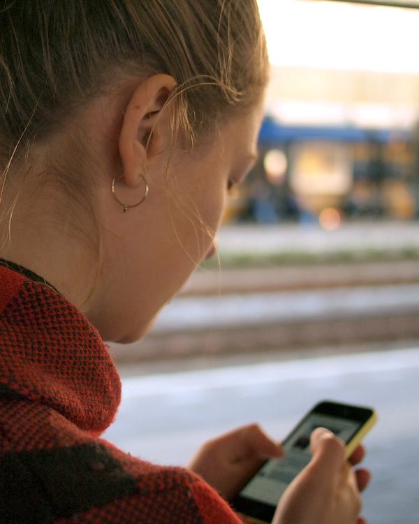 Woman in a red sweater checks her phone on a train platform