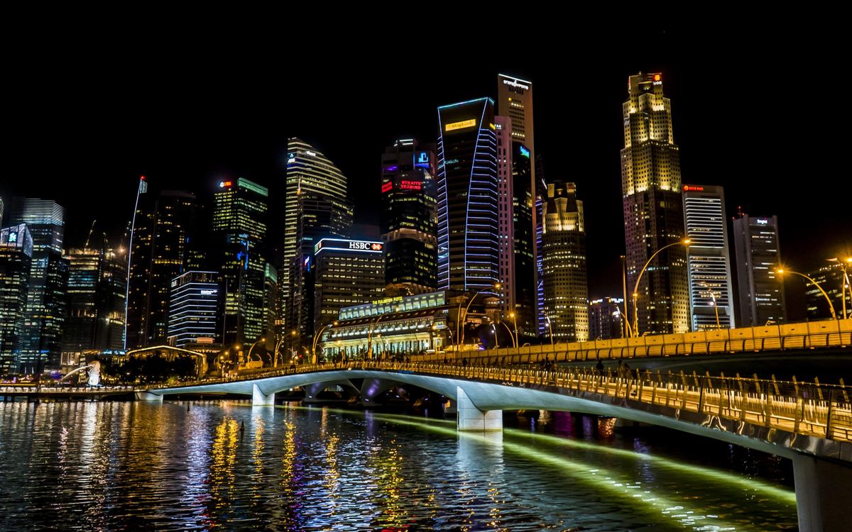 City skyline and a lit footbridge reflected in the water at night