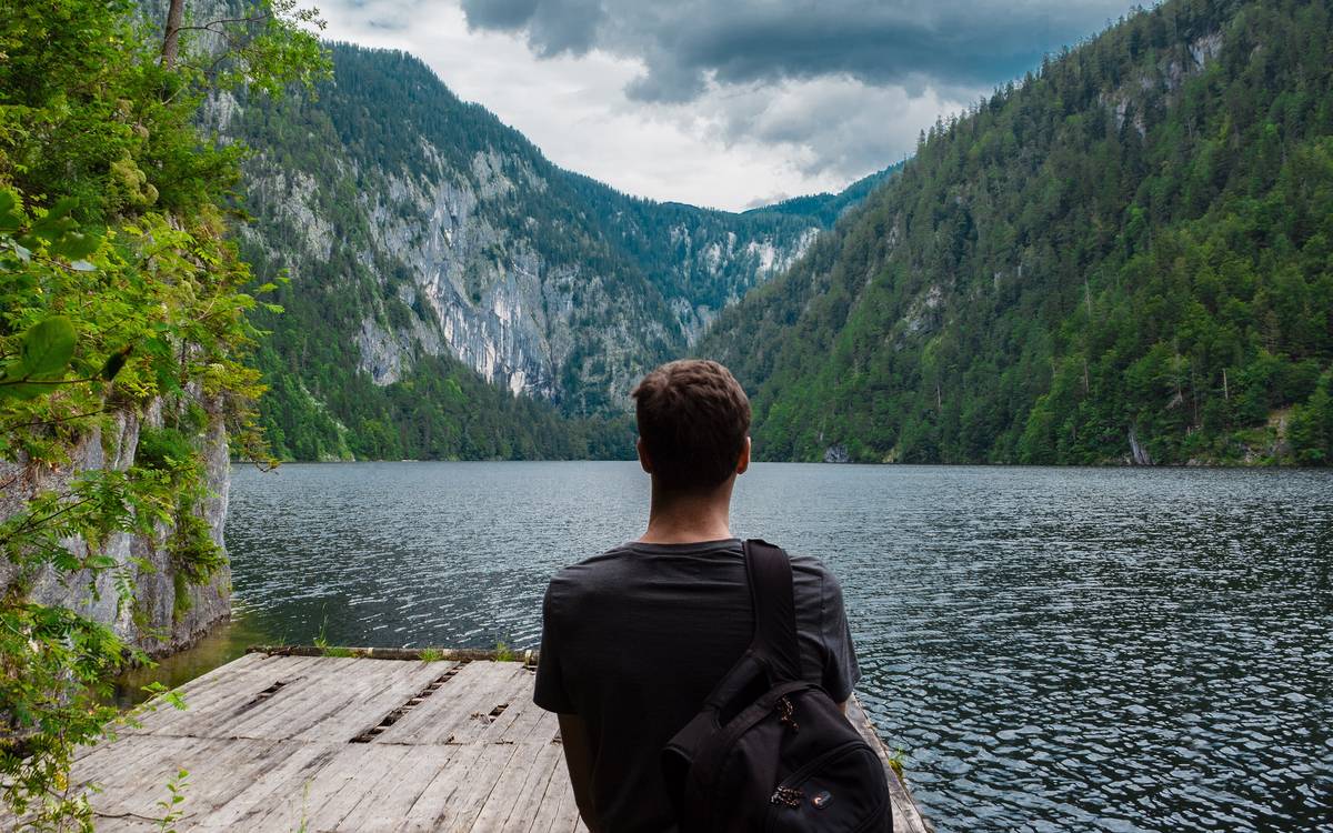 Man sitting at the end of a wooden platform looking over a mountain lake