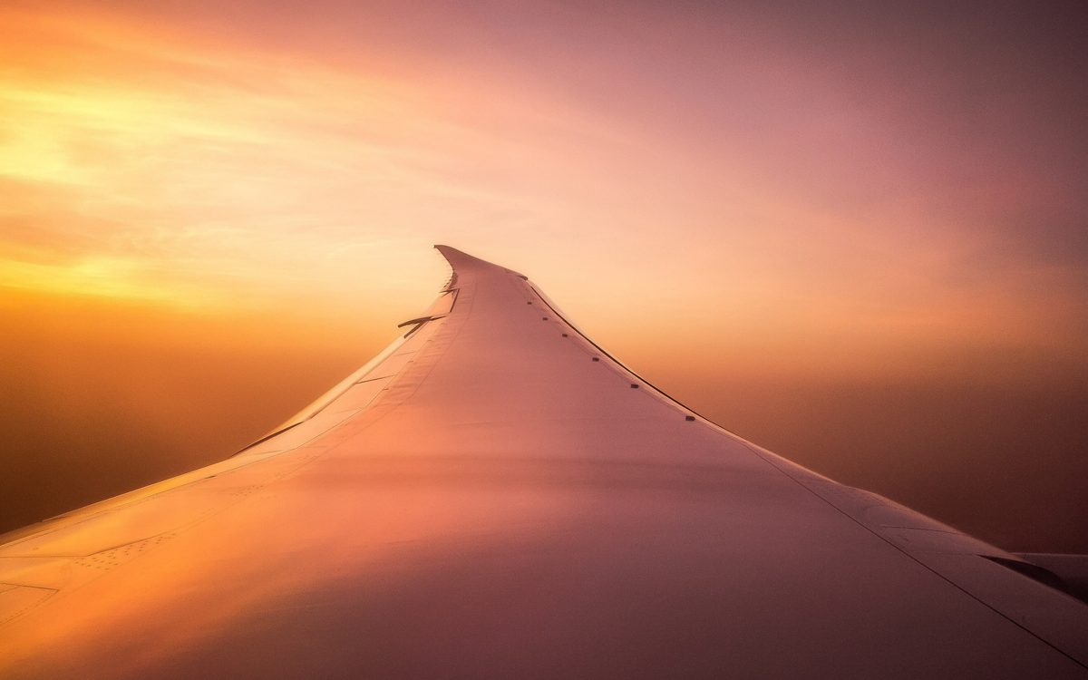 Airplane wing above the clouds in an orange sunset