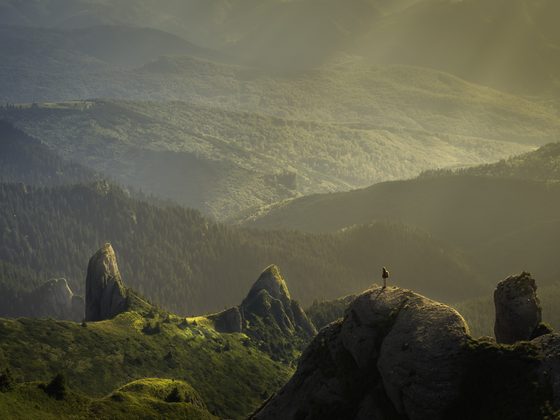 Lone hiker on a rock above a misty green valley
