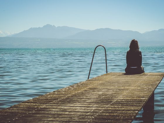Woman sitting at the end of a wooden pier on a calm lake