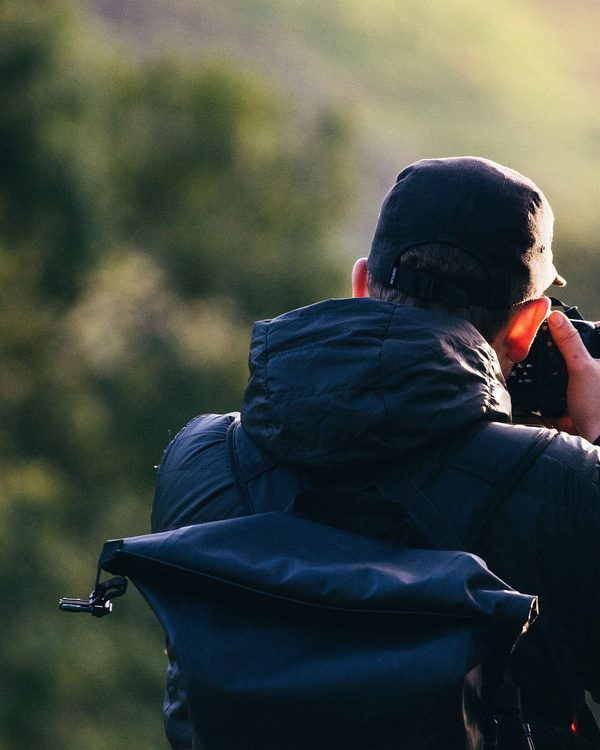 A photographer seen from behind raising a camera toward a green hillside