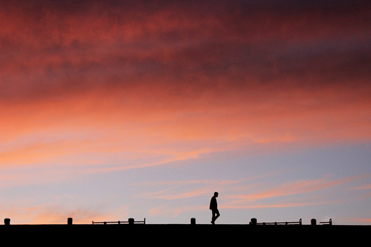 A lone walker in silhouette on a ridge under a red evening sky