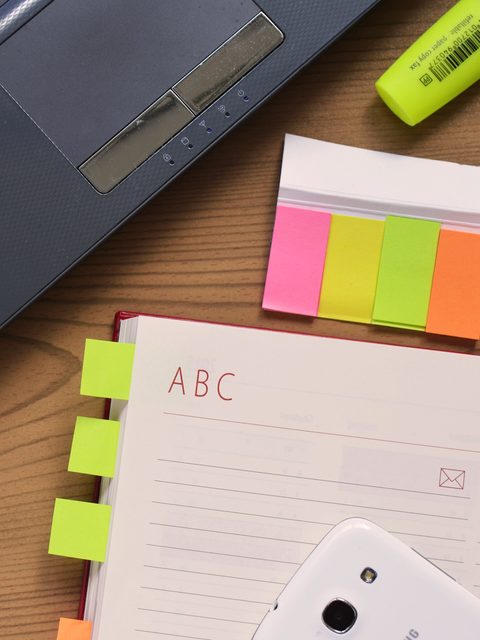 A laptop, a notebook and bright sticky notes on a wooden desk