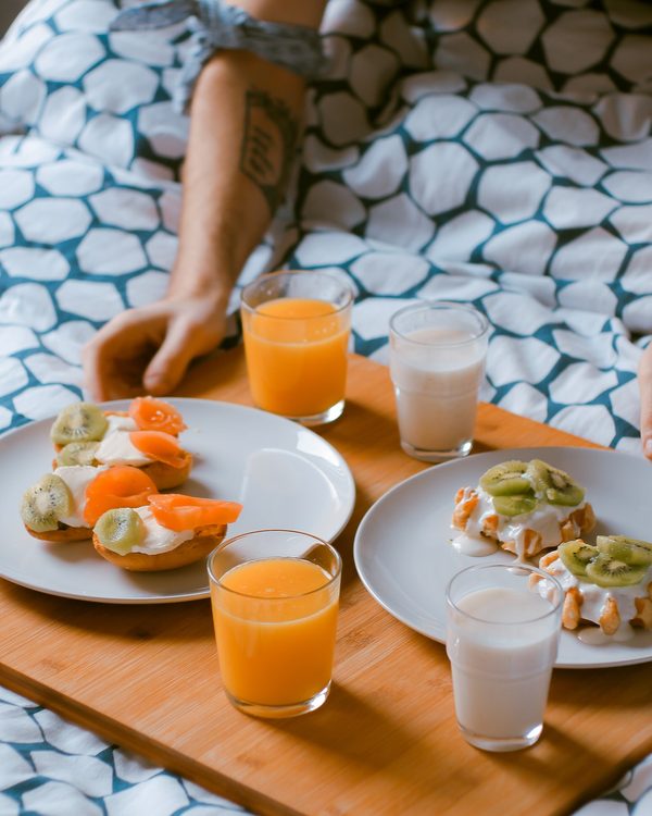 A wooden breakfast tray with toast, orange juice and milk on a patterned bed