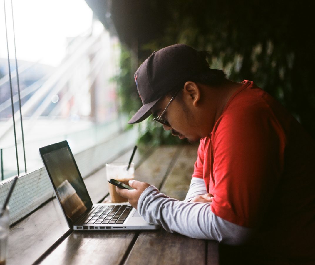 Man in a red shirt working on a laptop by a large window