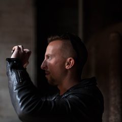 Man in a leather jacket taking a photo in low light