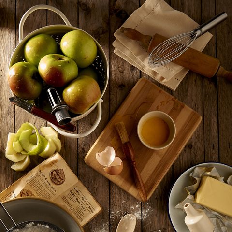 Apples, butter, eggs and a rolling pin laid out on a wooden table