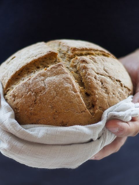 Two hands holding a round loaf of crusty bread in a linen cloth