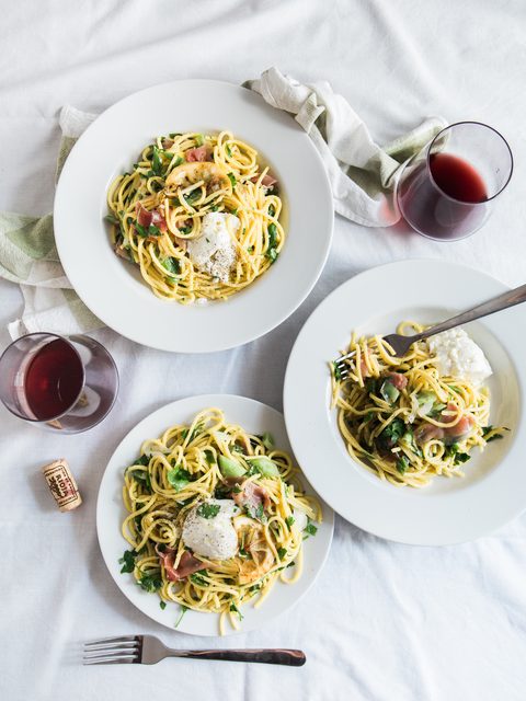Three plates of spaghetti with burrata and red wine on a white cloth