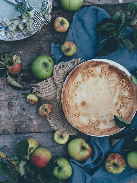A golden apple pie on a rustic table with green apples and a blue cloth