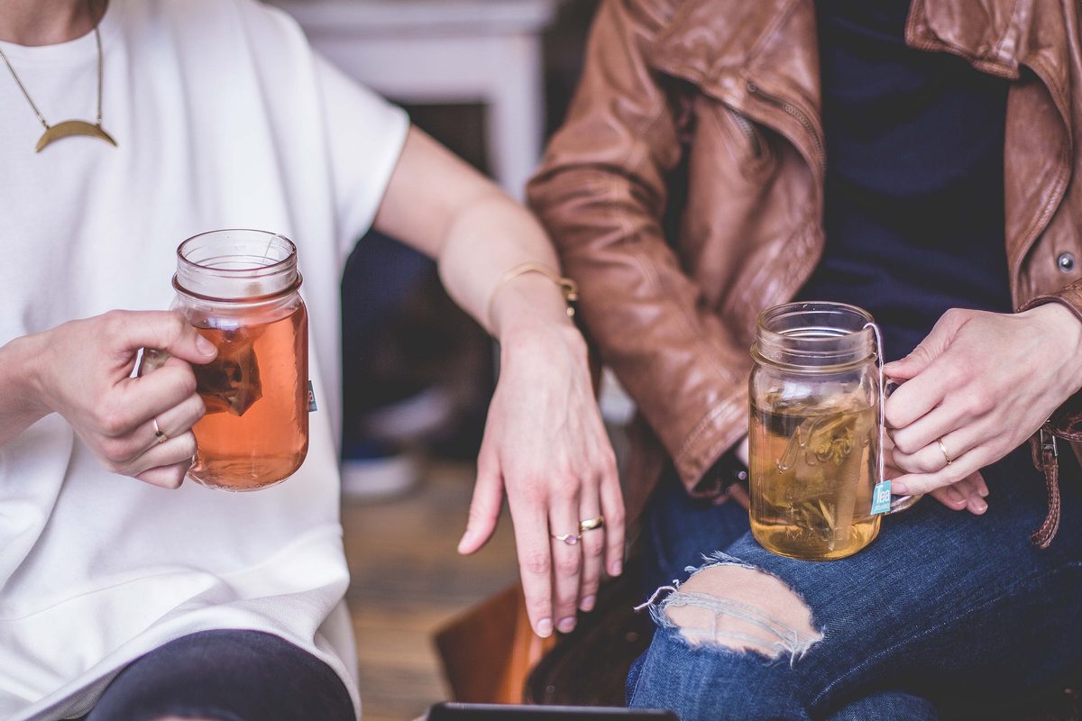 Two friends sit side by side holding glasses of iced tea