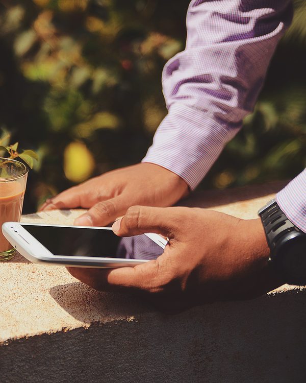 A man taps on his phone at a sunny outdoor table next to an iced coffee