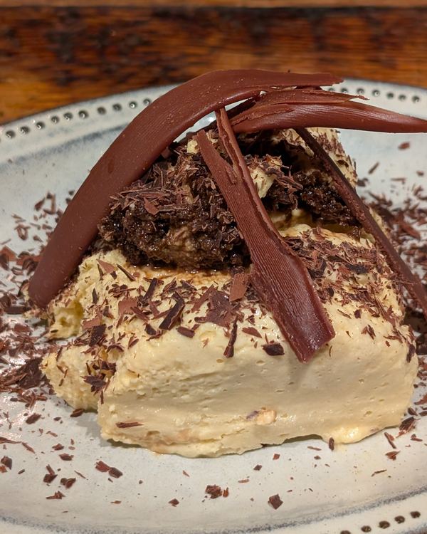 A chocolate and cream dessert with dark chocolate curls on a speckled plate
