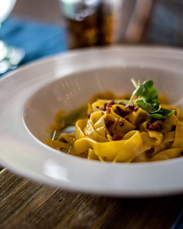 A bowl of golden tagliatelle with herbs on a dark wooden table