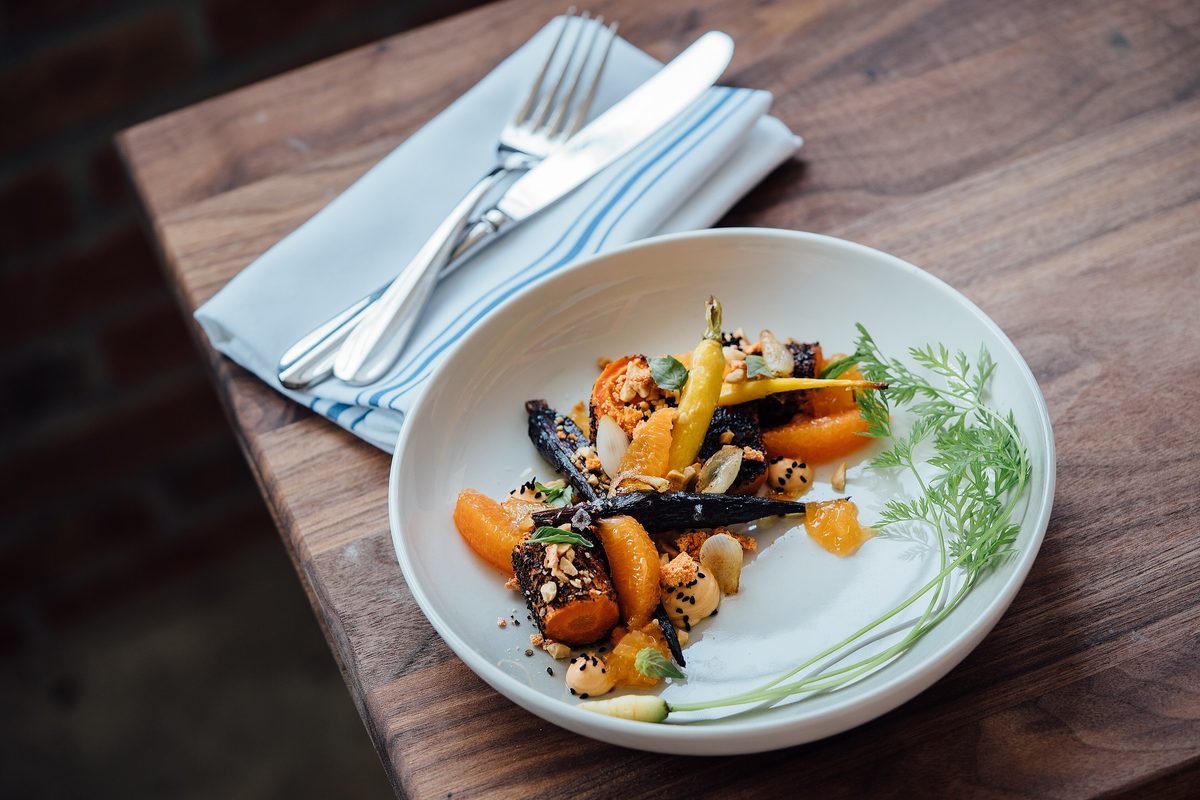 Roasted heirloom carrots with herbs in a white bowl on a dark wooden table