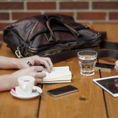Two people at a wooden table with a notebook, coffee and a tablet