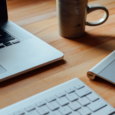 Open laptop, keyboard and a coffee mug on a warm wooden desk