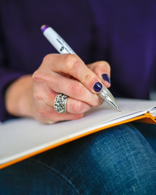 A person writes notes with a pen in an open notebook on their lap