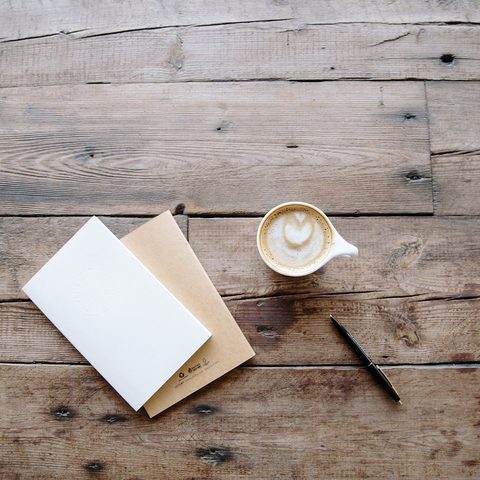 Two notebooks, a pen and a cup of coffee on a rustic wooden table
