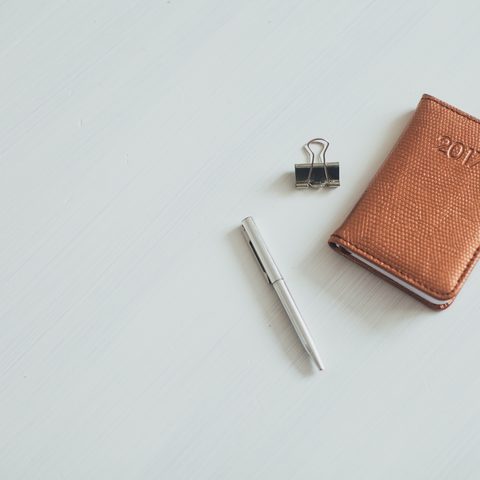 A brown notebook, a pen and a binder clip on a white desk