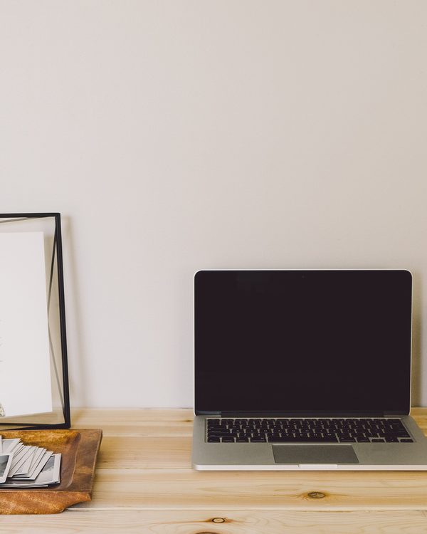 A laptop on a light wooden desk beside a small cactus and a picture frame