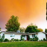Low white house with a green lawn under an orange evening sky