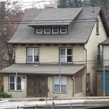 Two storey beige house with a porch on a hillside street