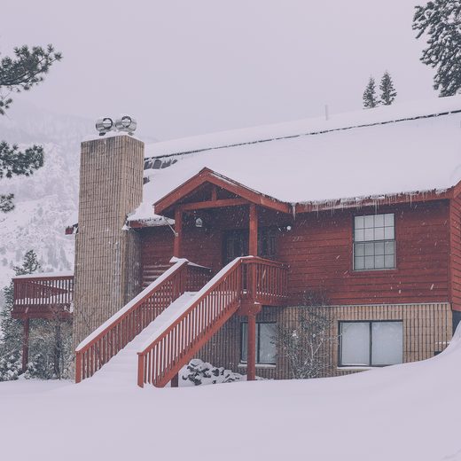 Red wooden chalet with a snowy roof and a stone chimney