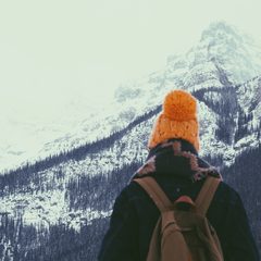 Hiker in an orange beanie looking at snowy mountains