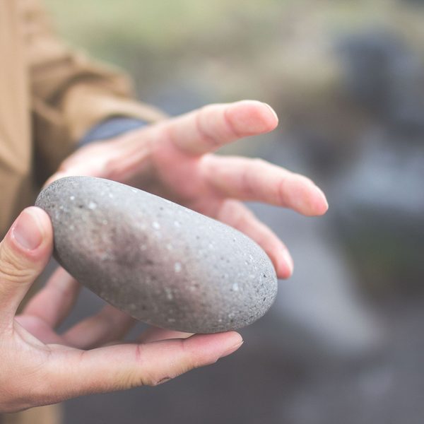 A hand holding a smooth grey stone