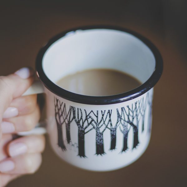 A hand holds an enamel mug of hot tea with a forest print