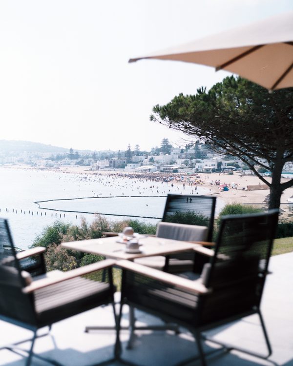 Chairs and a table under a sun umbrella on a terrace above the beach