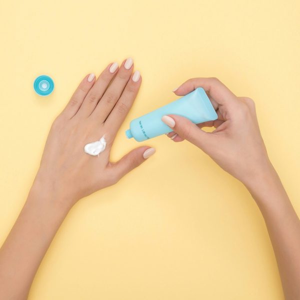 Hands rubbing in white cream from a pale blue tube on a yellow table