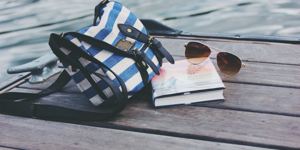 Blue and white striped beach bag on a wooden dock with sunglasses