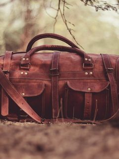 Brown leather duffel bag on dry grass