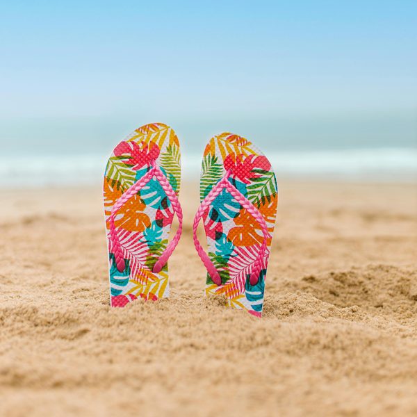 A pair of bright tropical print flip flops standing in beach sand