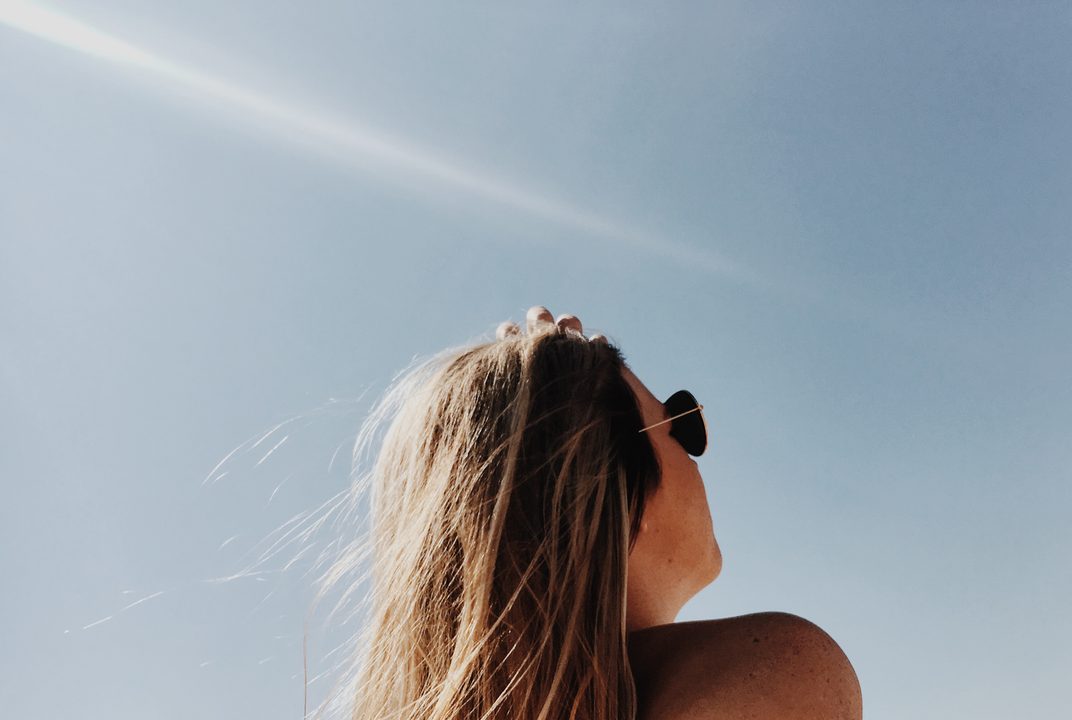 A woman in sunglasses looks up at a clear blue summer sky