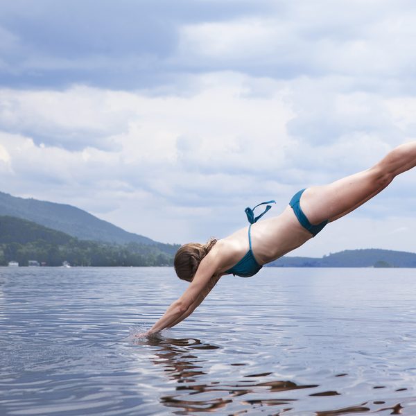 A swimmer in a teal bikini dives into a calm lake