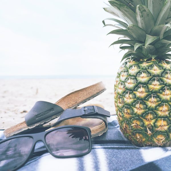 Sunglasses and sandals beside a pineapple on a beach blanket