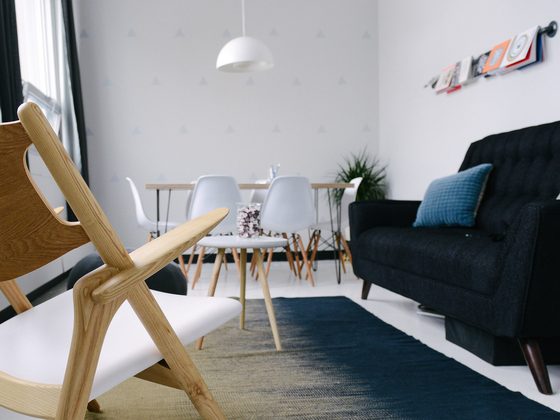 Bright lounge corner with a wooden chair, dark sofa and white dining chairs