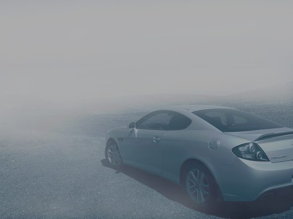A silver coupe parked on a quiet road in thick morning fog