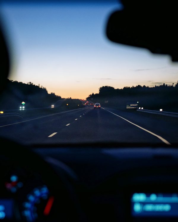 View through a car windshield of an empty highway at dusk with a glowing dashboard