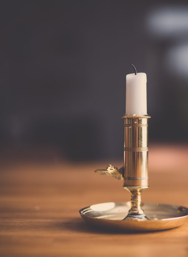 A white candle in a brass holder on a warm wooden table