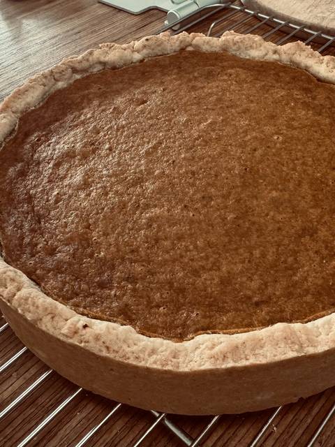 A whole pumpkin pie with a crimped crust cooling on a wire rack