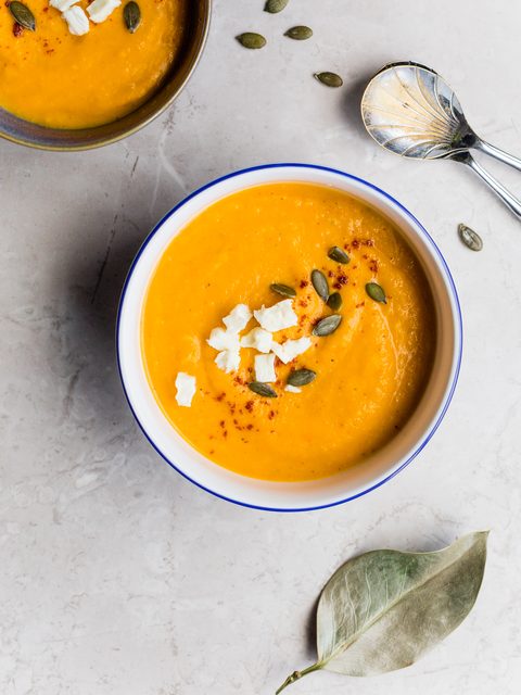 Two bowls of orange squash soup topped with feta and pumpkin seeds