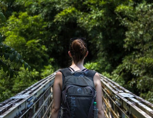 Hiker with a backpack crossing a wooden bridge in a green forest